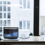 Sleek office desk setup featuring a laptop, glass of water, and open window view.