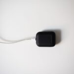 Black earbud case with charging cable on white background in minimalist style.