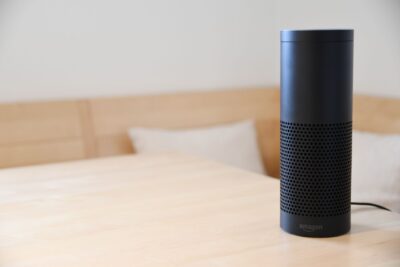 A black smart speaker resting on a light-colored wooden table in a cozy indoor setting.